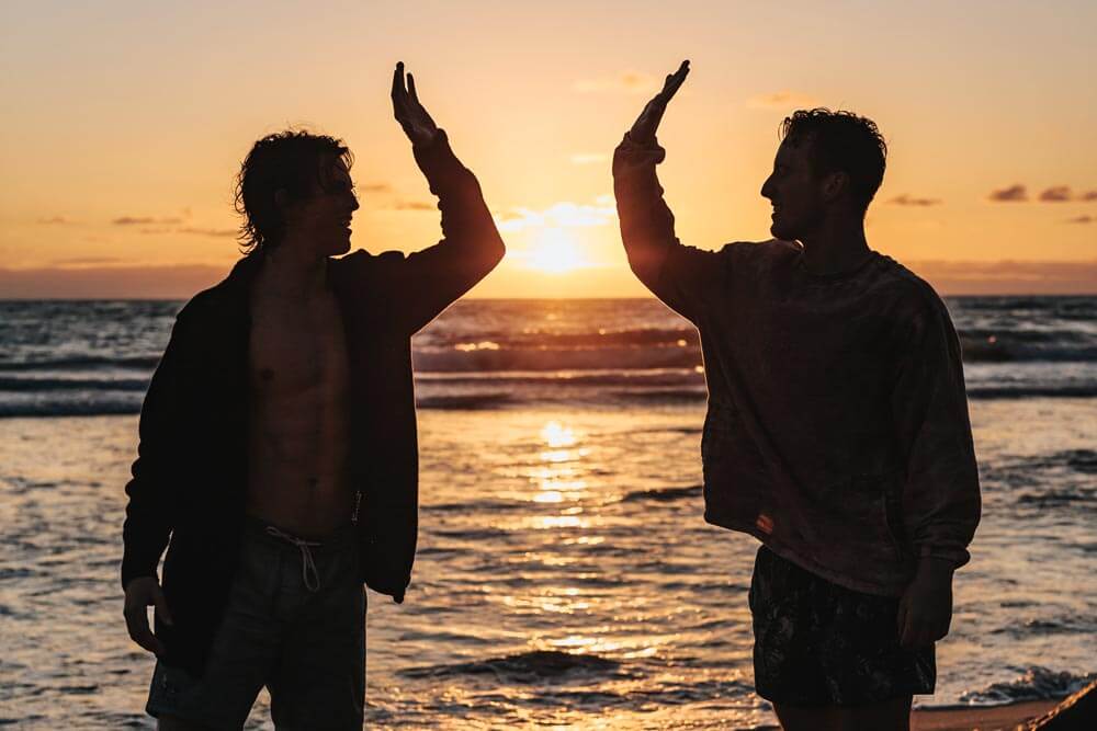 broadwaytreatmentcenter-7-Ways-to-Build-Self-Esteem-in-Recovery-photo-of-two-friends-doing-high-five-at-the-beach